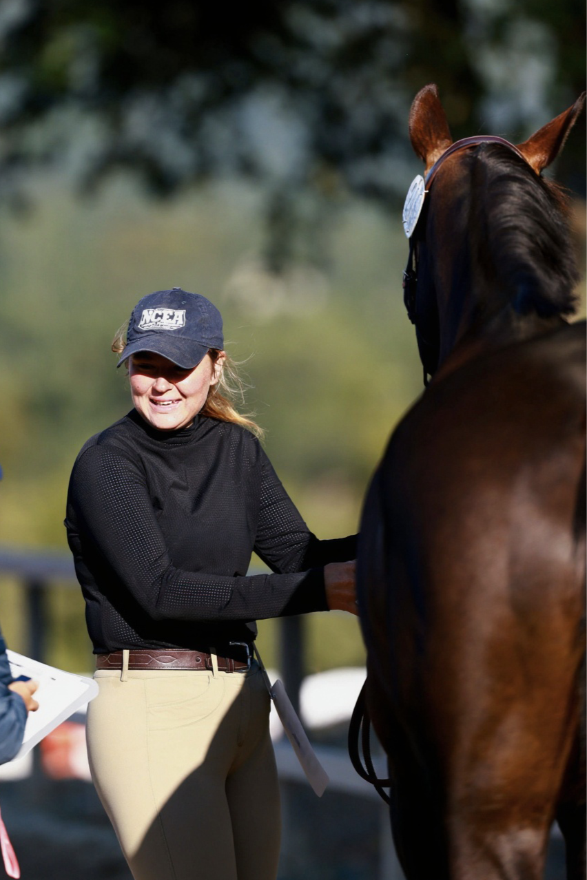 Cecily Hayes wearing riding breeches and smiling at her horse who has just completed a Jog for a competition